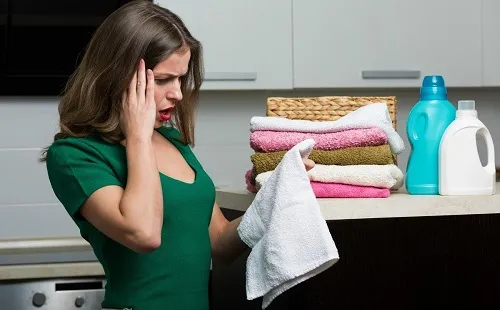 Девушка в зеленом платье видит пятна на своих полотенцах после стирки в стиральной машине