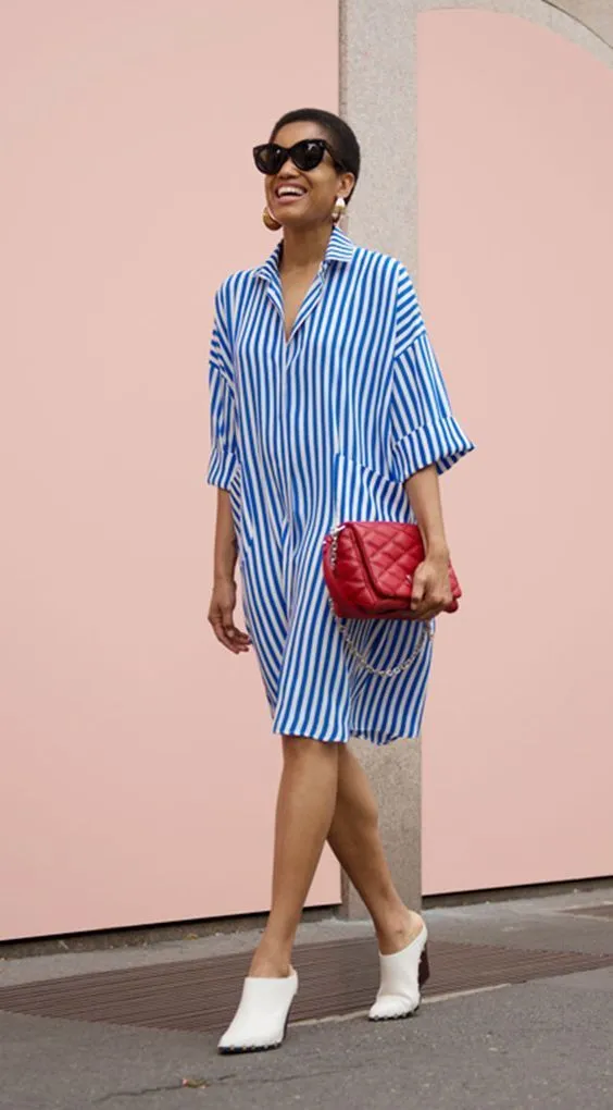 Свободное синее платье в полоску с рубашкой сочетается с белыми туфлями-сабо и красной сумкой.