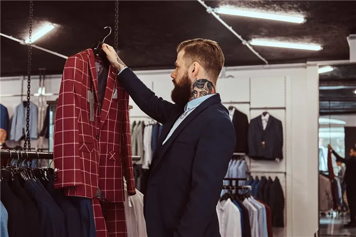 Элегантно одетый бородатый мужчина выбирает клетчатый пиджак