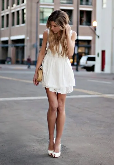 Девушка в коротком белом платье и с маленькой сумкой