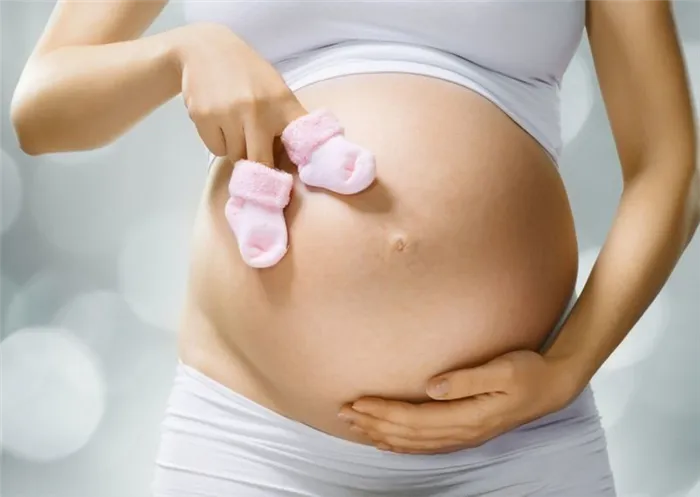 Беременная женщина держит детские носочки рядом с животиком.