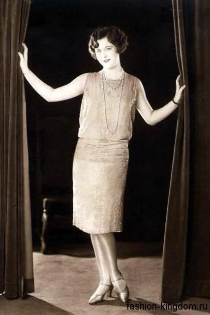 Модное платье 1920 годов прямого кроя, длиной миди, без рукавов в сочетании с ниткой жемчуга и туфлями на низком каблуке.