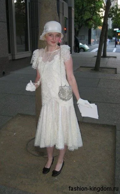 Белое платье-миди в стиле 1920, прямого кроя, украшенное ажурными вставками, в тандеме с ниткой жемчуга и шляпой клош.