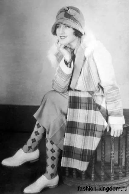 Длинное пальто в клетку 1920 годов, прямого кроя, с меховым воротником в тандеме со шляпой клош и туфлями в мужском стиле.