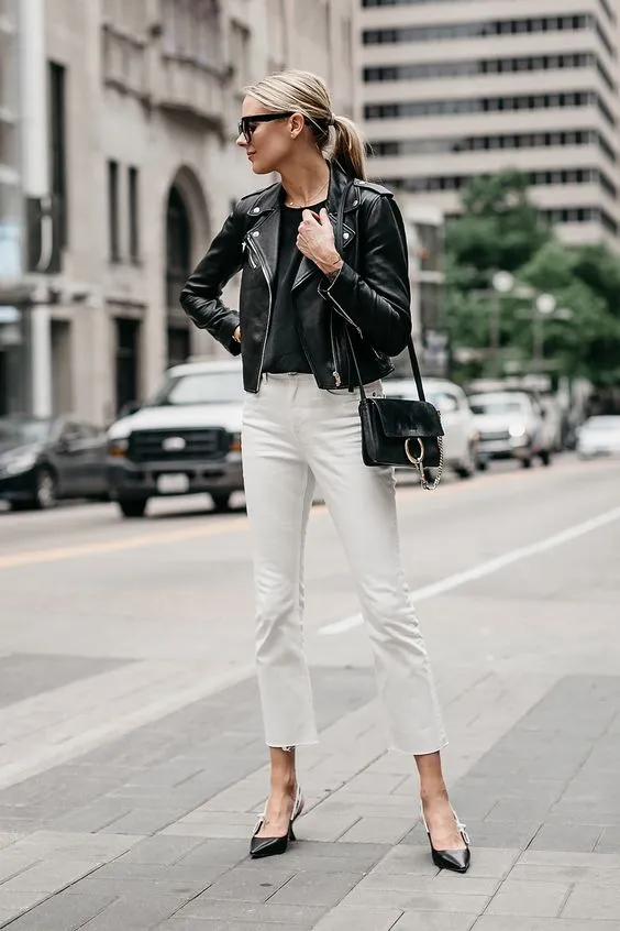 На девушке черный топ и кожаная куртка, белые прямые джинсы и черные туфли на невысоком каблуке, черная поясная сумка и очки.